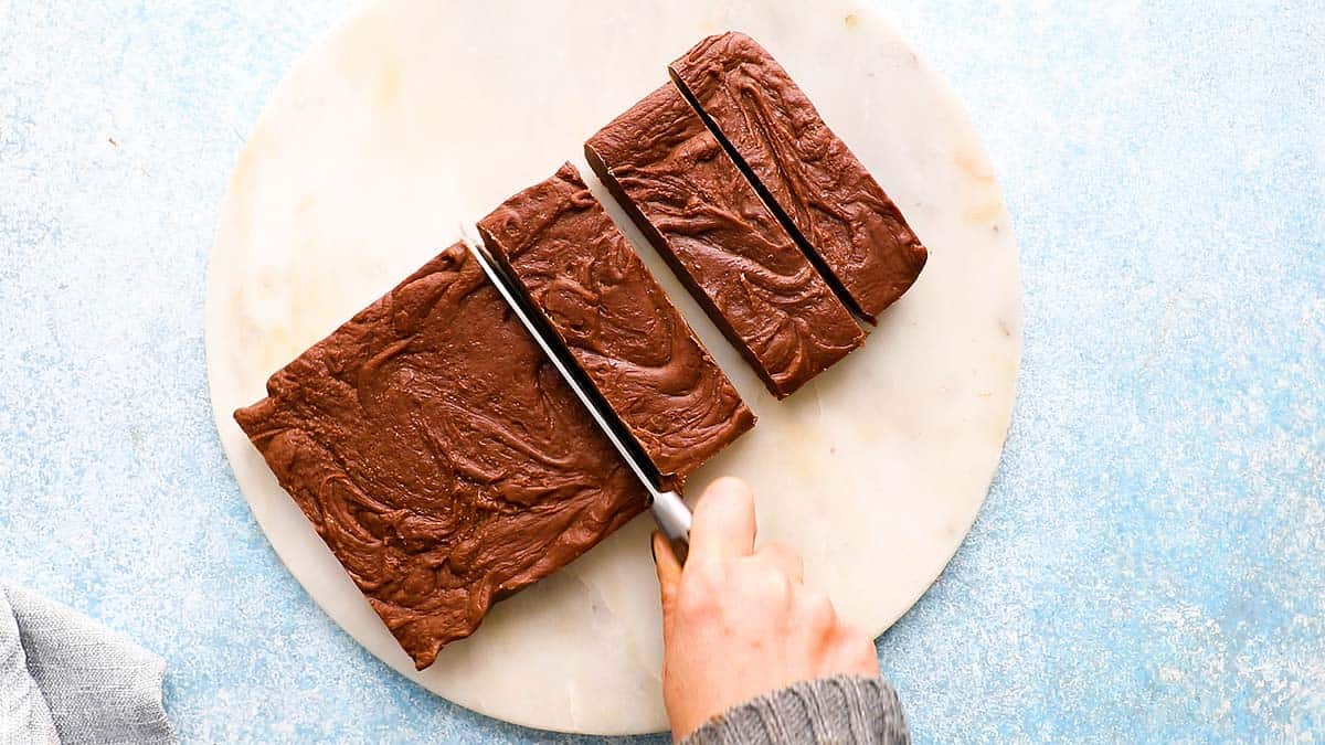 a hand cutting a set peanut butter fudge into slices.