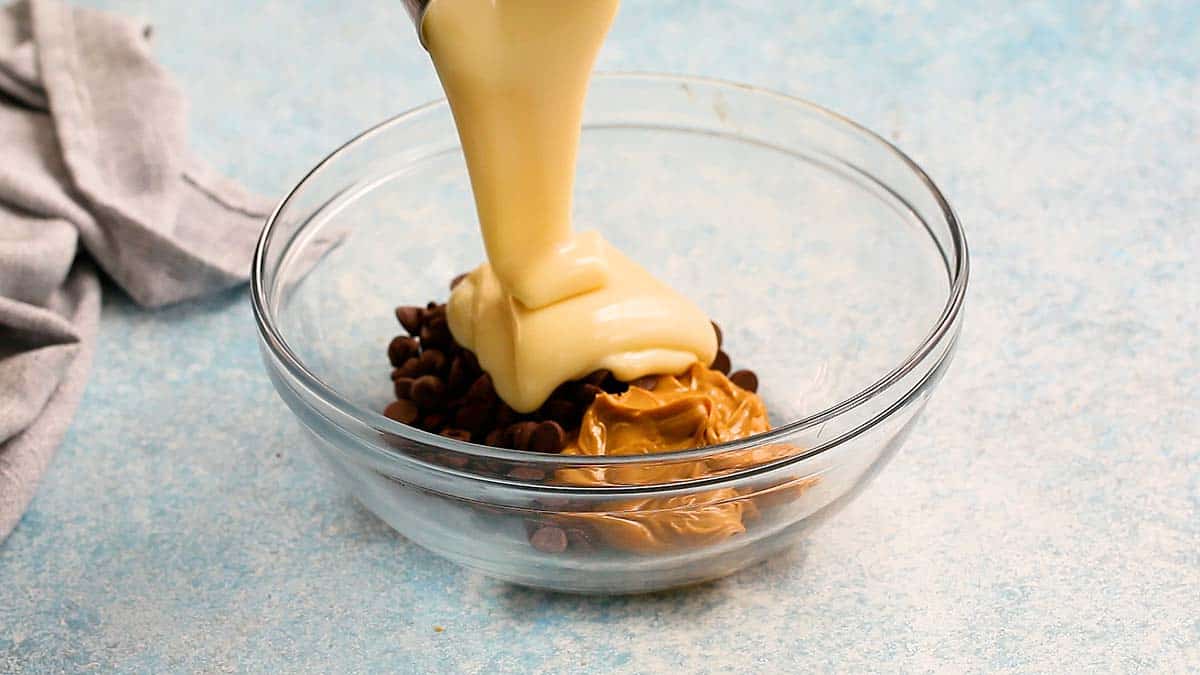 sweetened condensed milk is being poured into a bowl with peanut butter and chocolate.