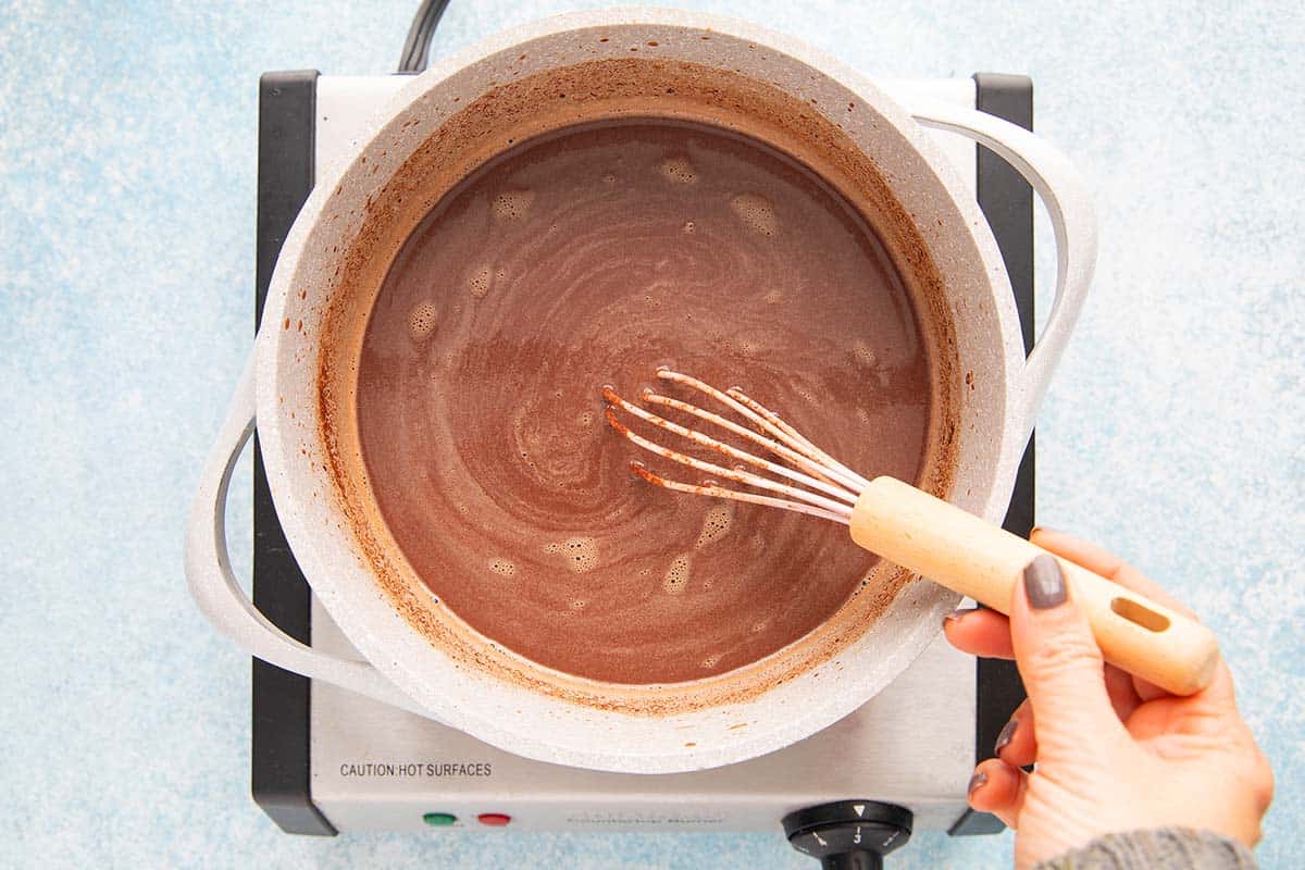 a hand whisking drinking chocolate in a sauce pan. 