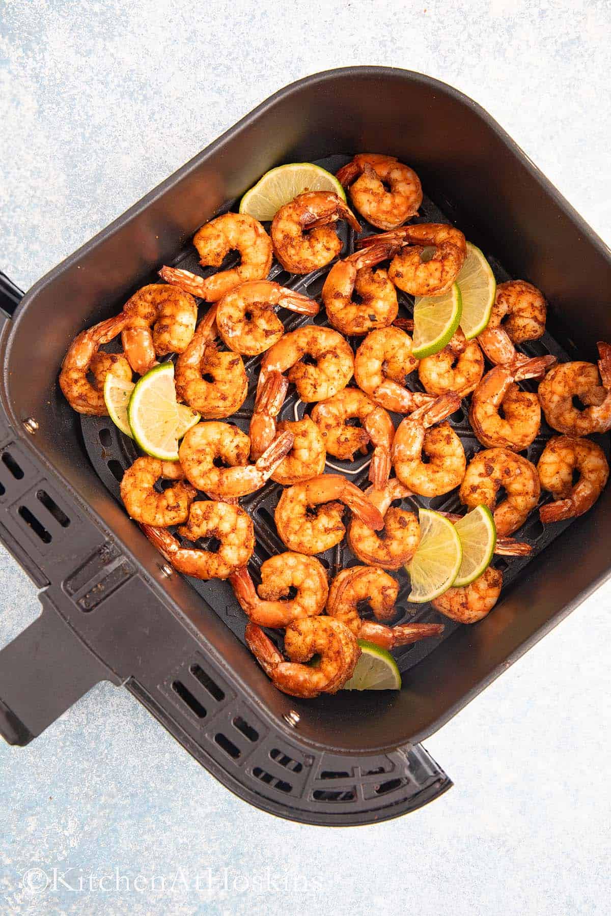 air fryer basket with cooked shrimp and garnished with lime wedges.