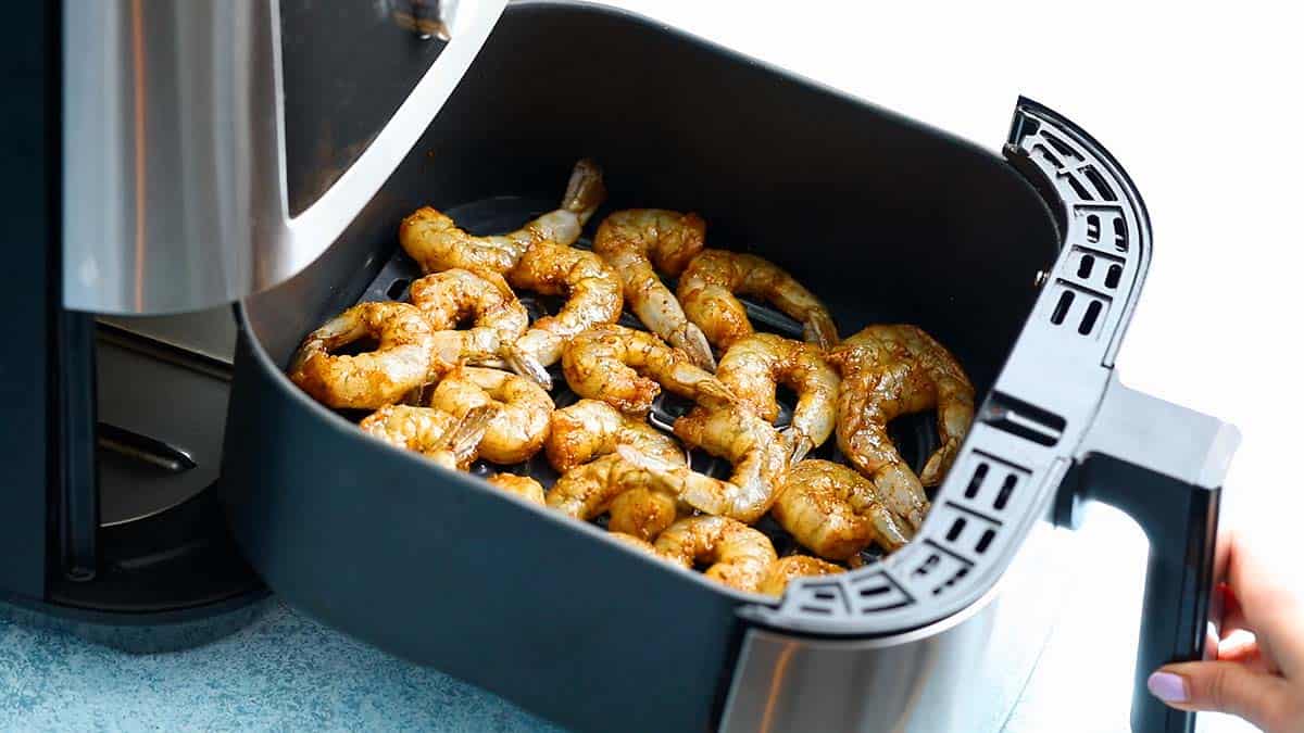 a hand closing an air fryer basket with seasoned shrimp.