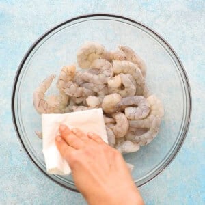 a hand holding a white paper above shrimp in a glass bowl.