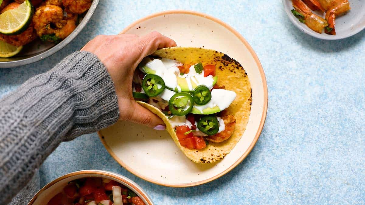 a hand removing an assembled taco from a plate.