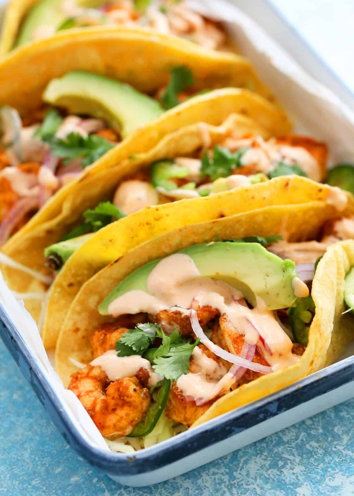 4 assembled shrimp tacos in a white tray.