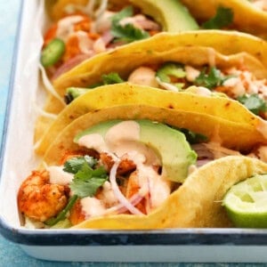 4 shrimp tacos assembled in a white tray.