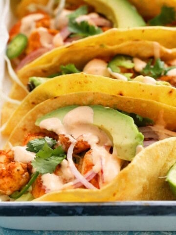 4 shrimp tacos assembled in a white tray.