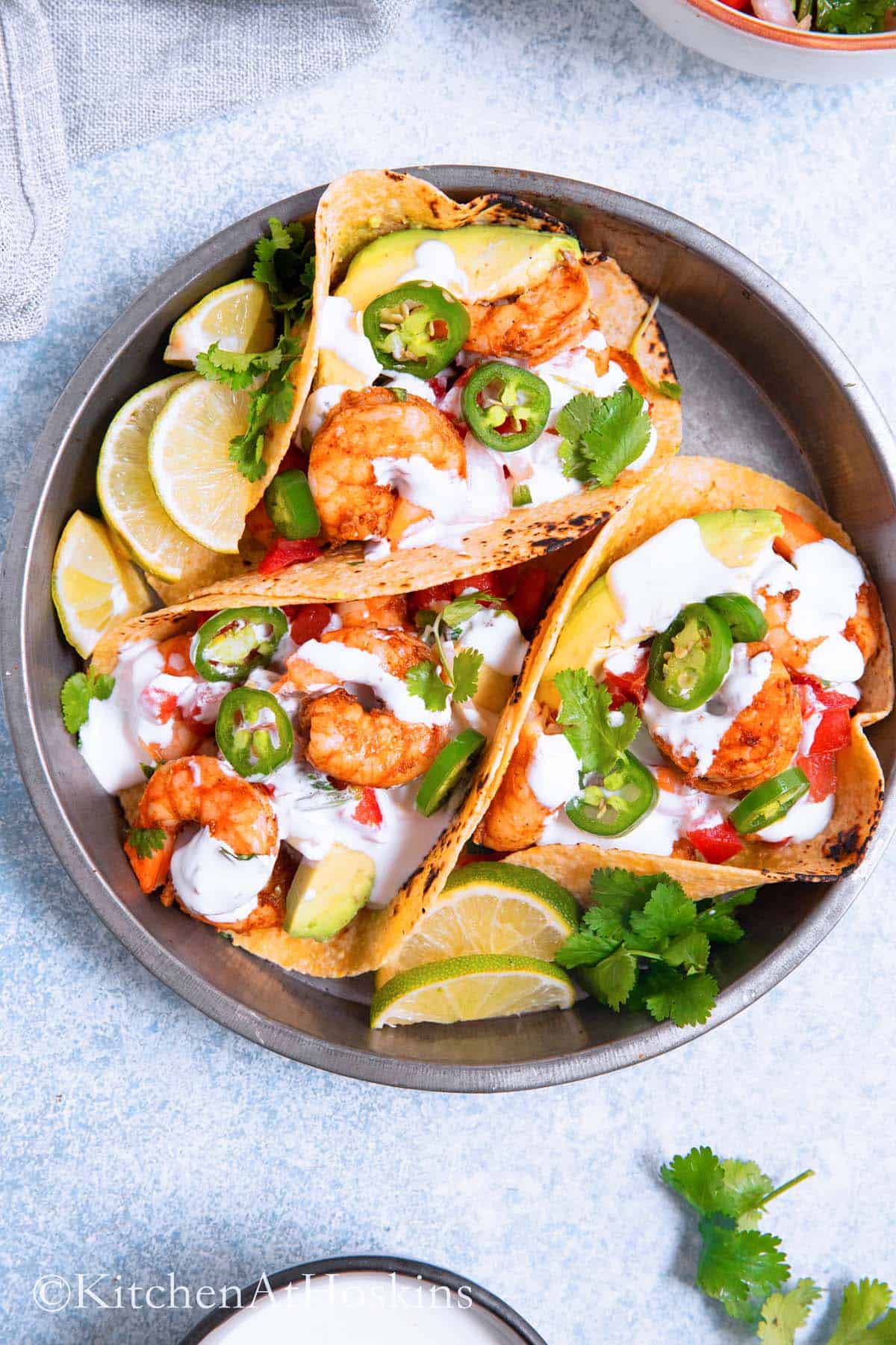 aluminum round platter containing three shrimp tacos with lime wedges.