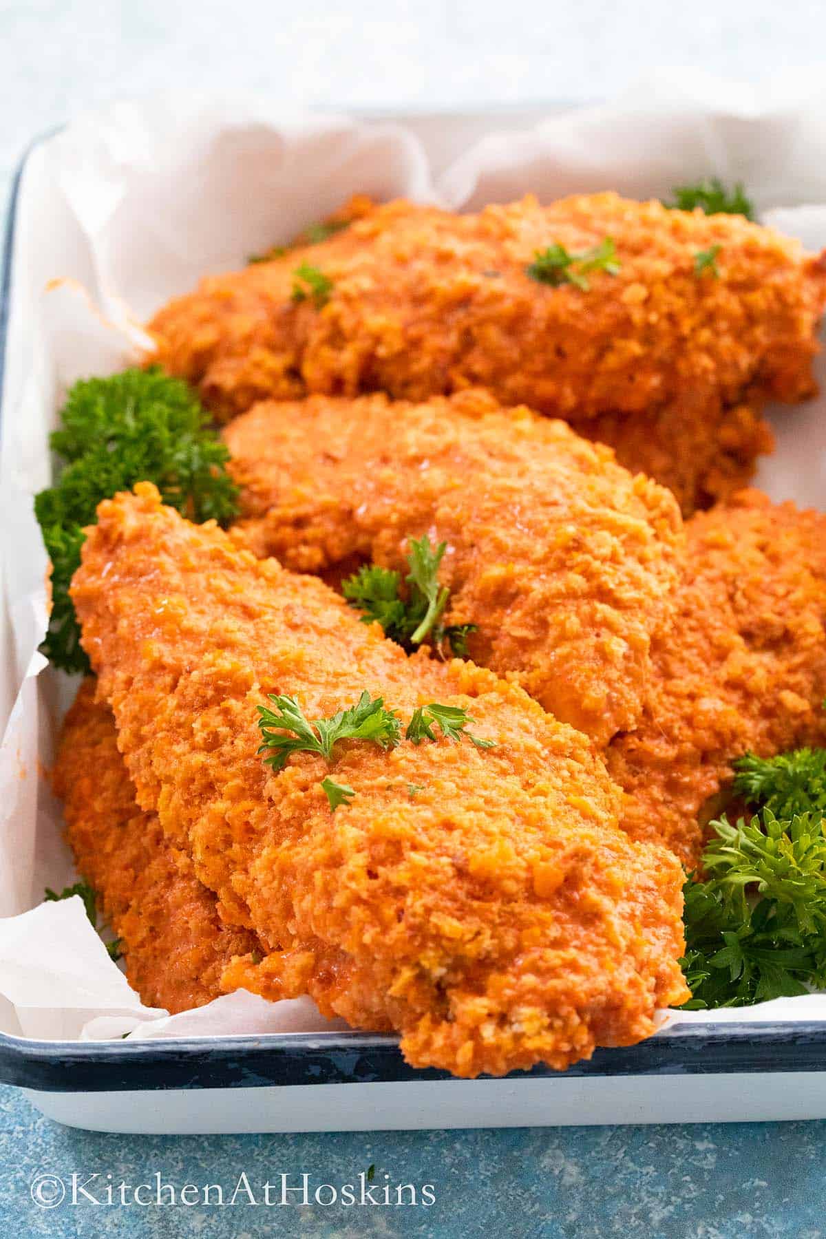 baked buffalo chicken tenders on a white tray garnished with parsley.