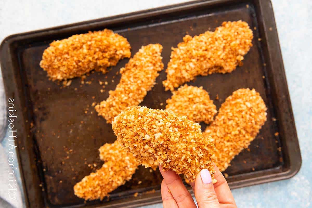 a hand holding a baked breaded chicken tender.