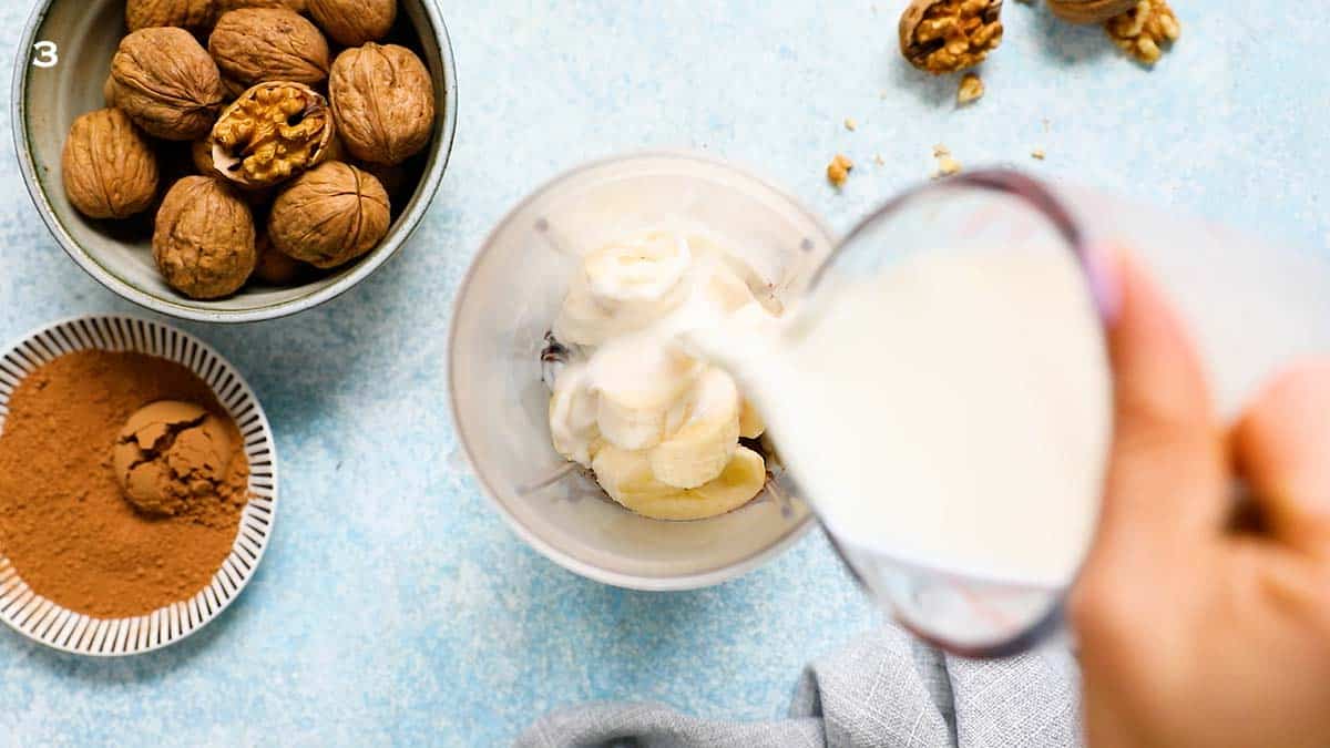 a hand pouring milk using a glass measuring cup into a blender.