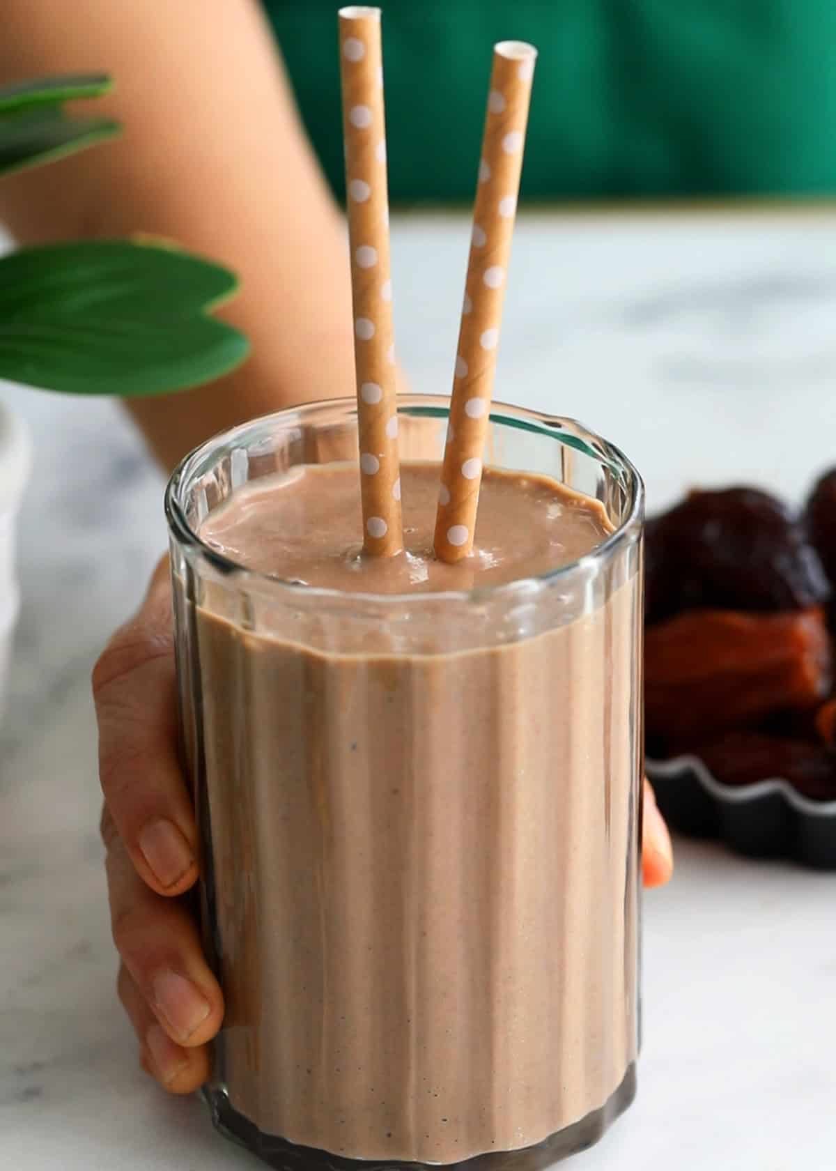 a hand holding a glass of date and walnut smoothie.