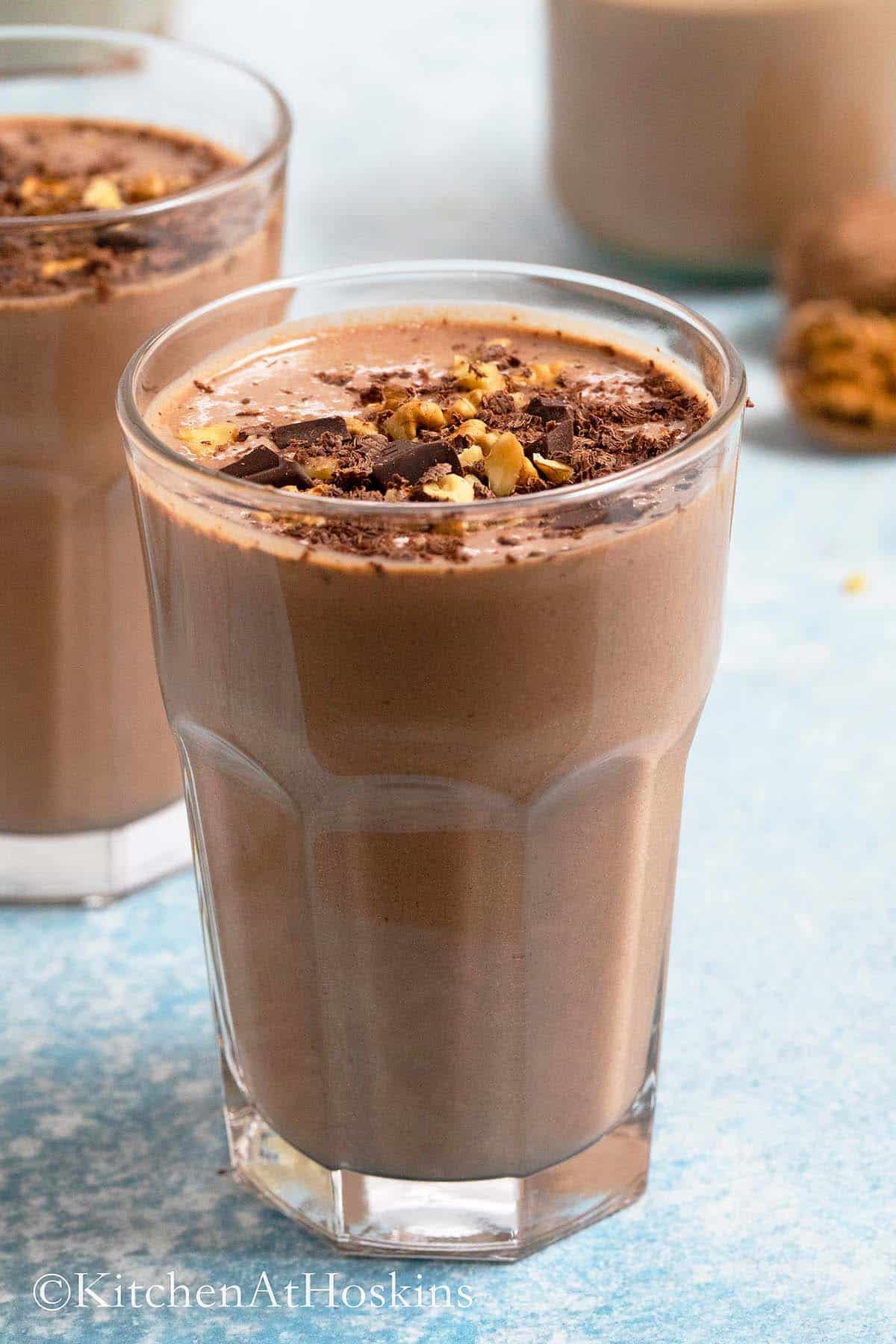 chocolate walnut smoothie in glasses topped with chopped walnuts.