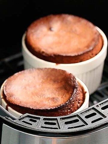 two chocolate cakes in a white ramekins in a air fryer basket.