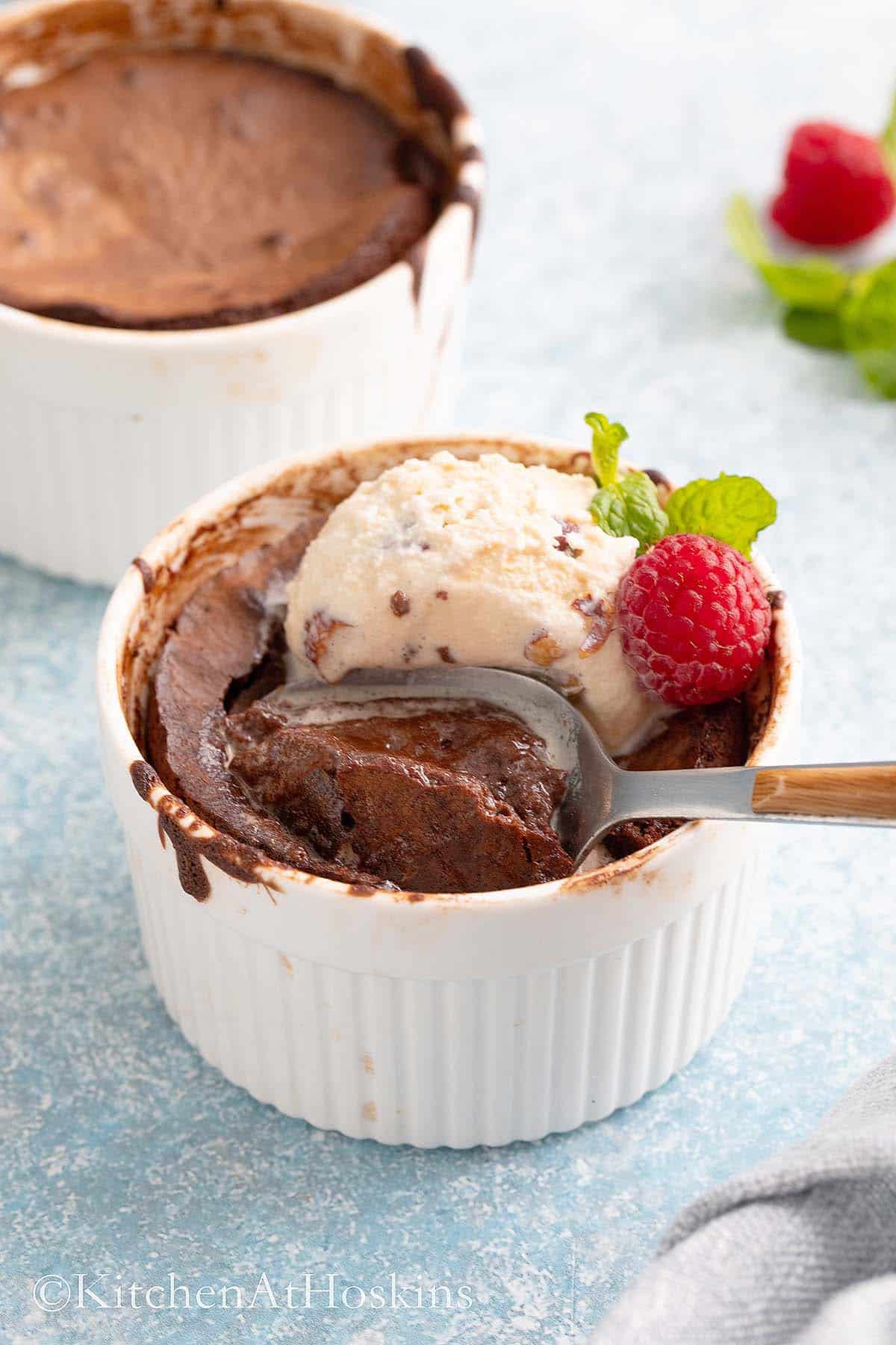 cooked lava cakes in two small ramekins, one with ice cream, mint, raspberry and a spoon.