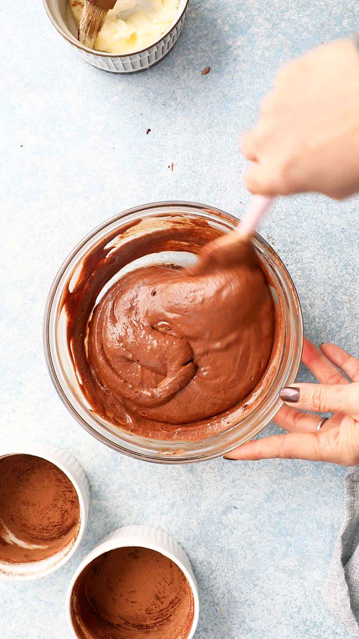 two hands folding chocolate cake batter with a pink spatula.