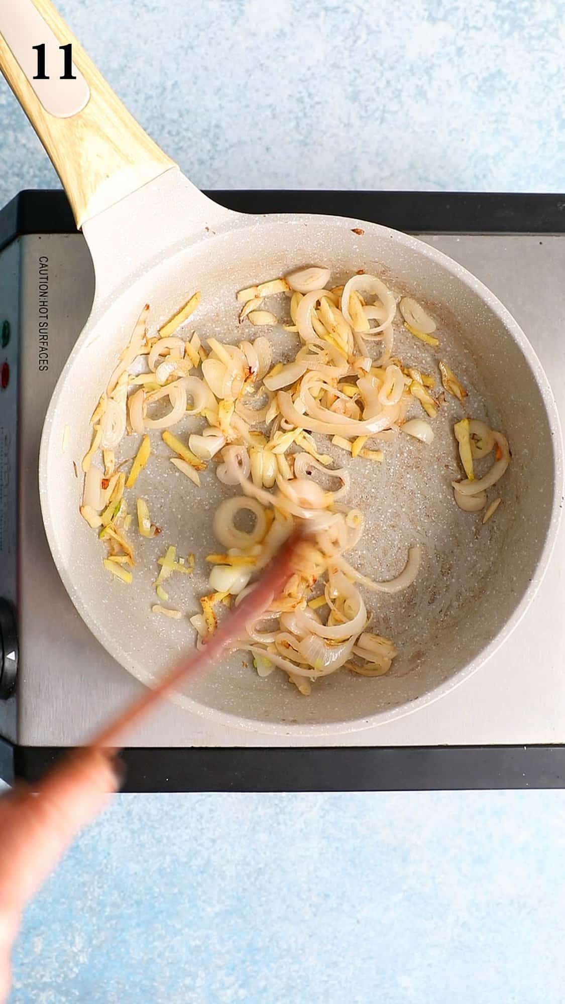 a hand sautéing sliced onion, ginger and garlic in a small skillet.