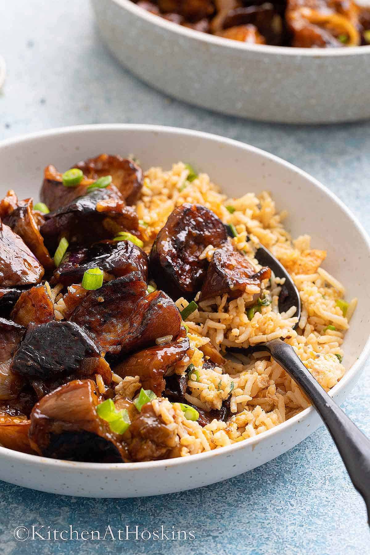 white bowl with fried rice, cooked eggplant and black fork.