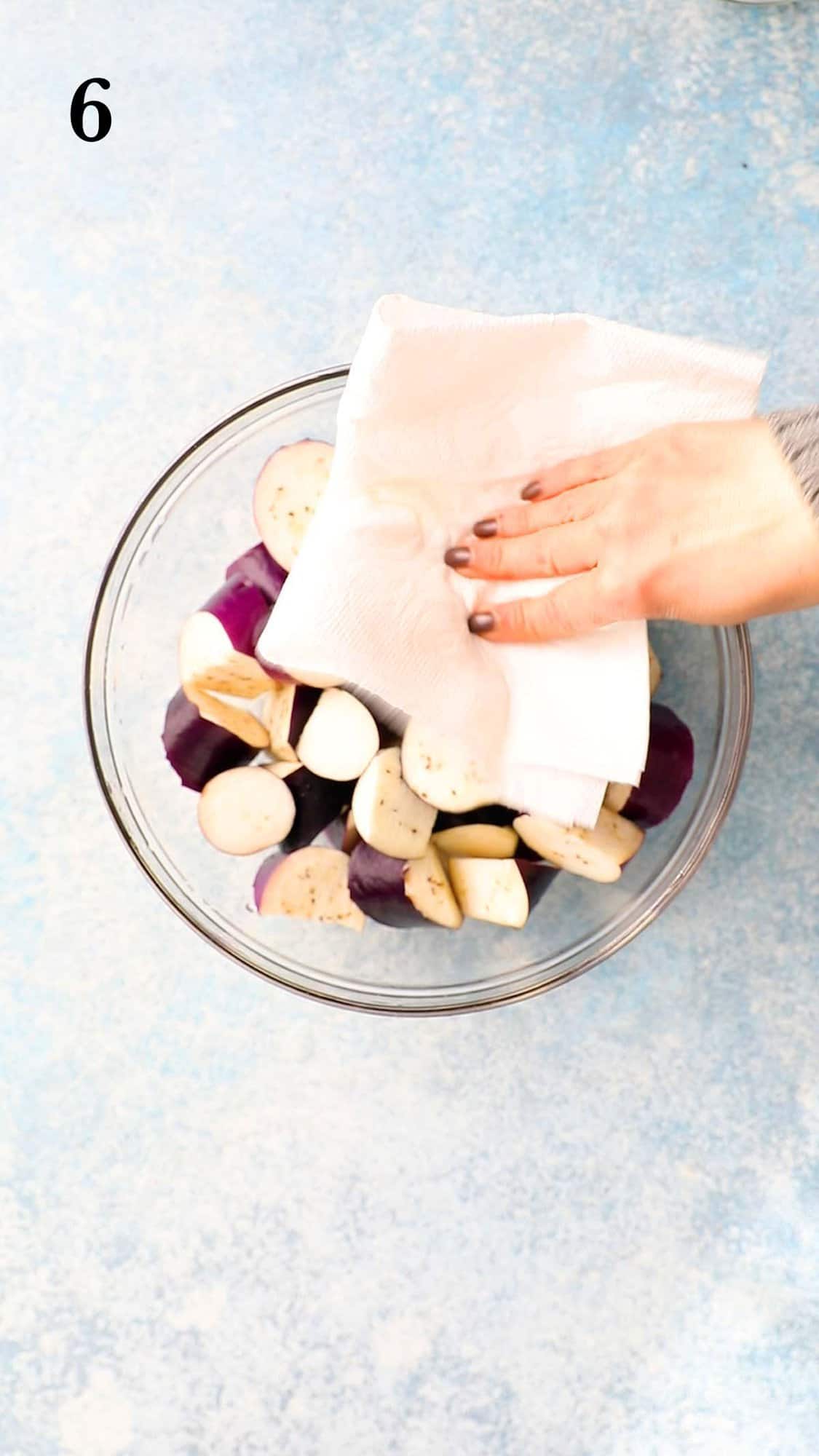 a hand drying eggplant chunks in a glass bowl with paper towel.