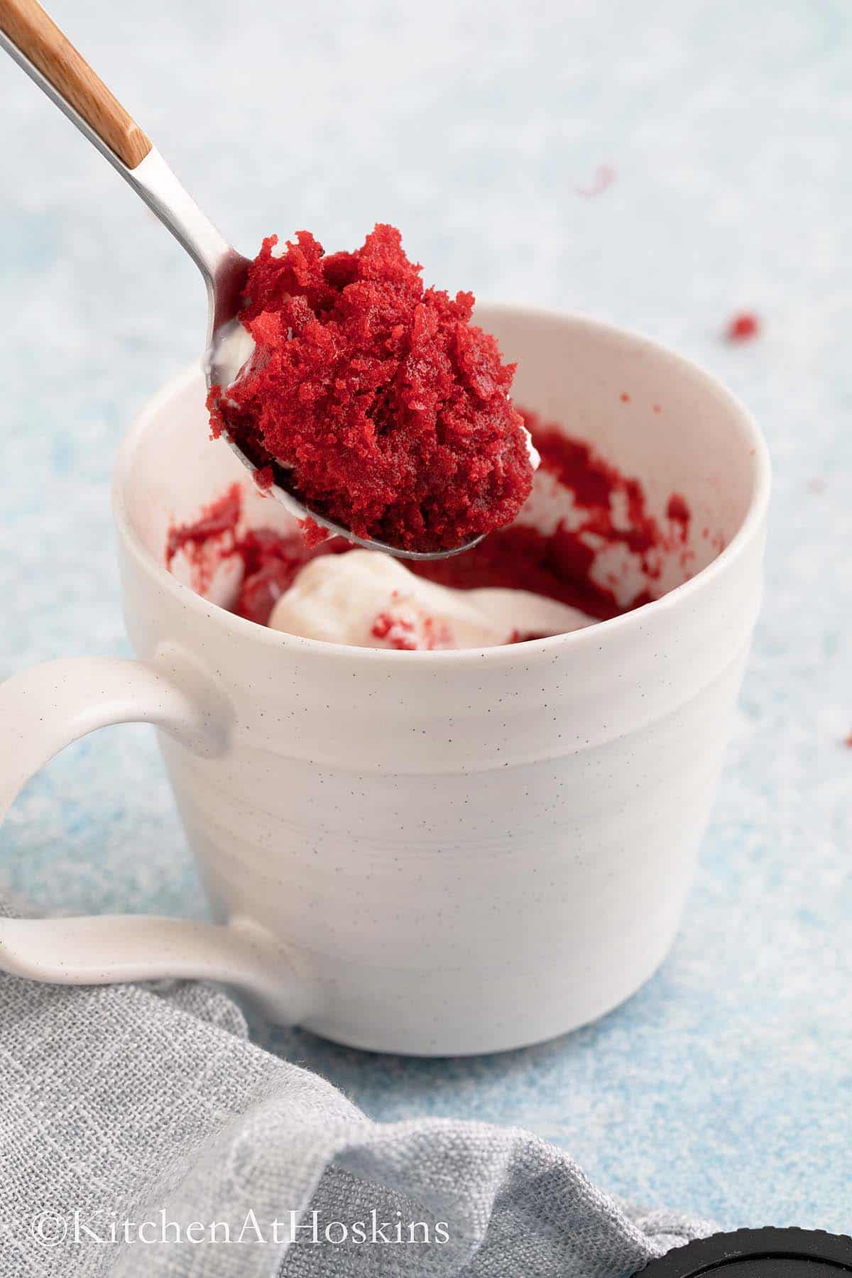 a spoonful of red velvet cake above a white mug.