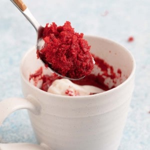 a spoonful of red velvet cake above a white cup.
