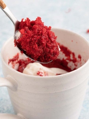 a spoonful of red velvet cake above a white cup.