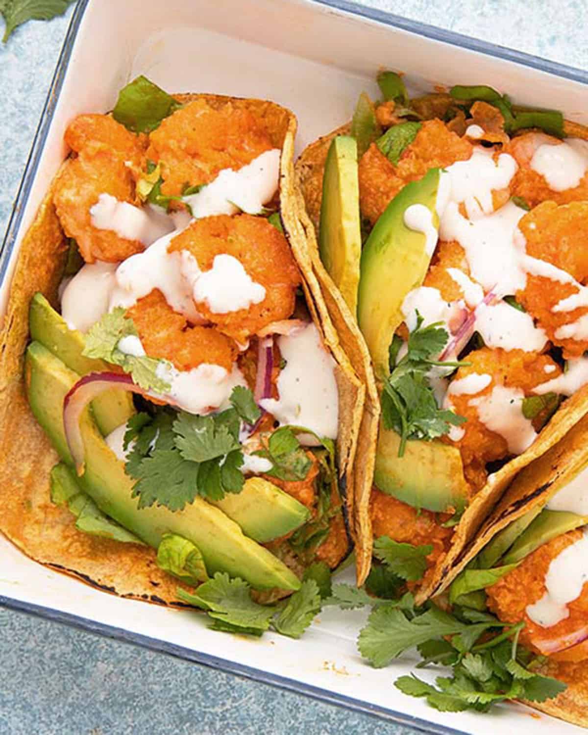two orange shrimp tacos with green avocado in a white platter.