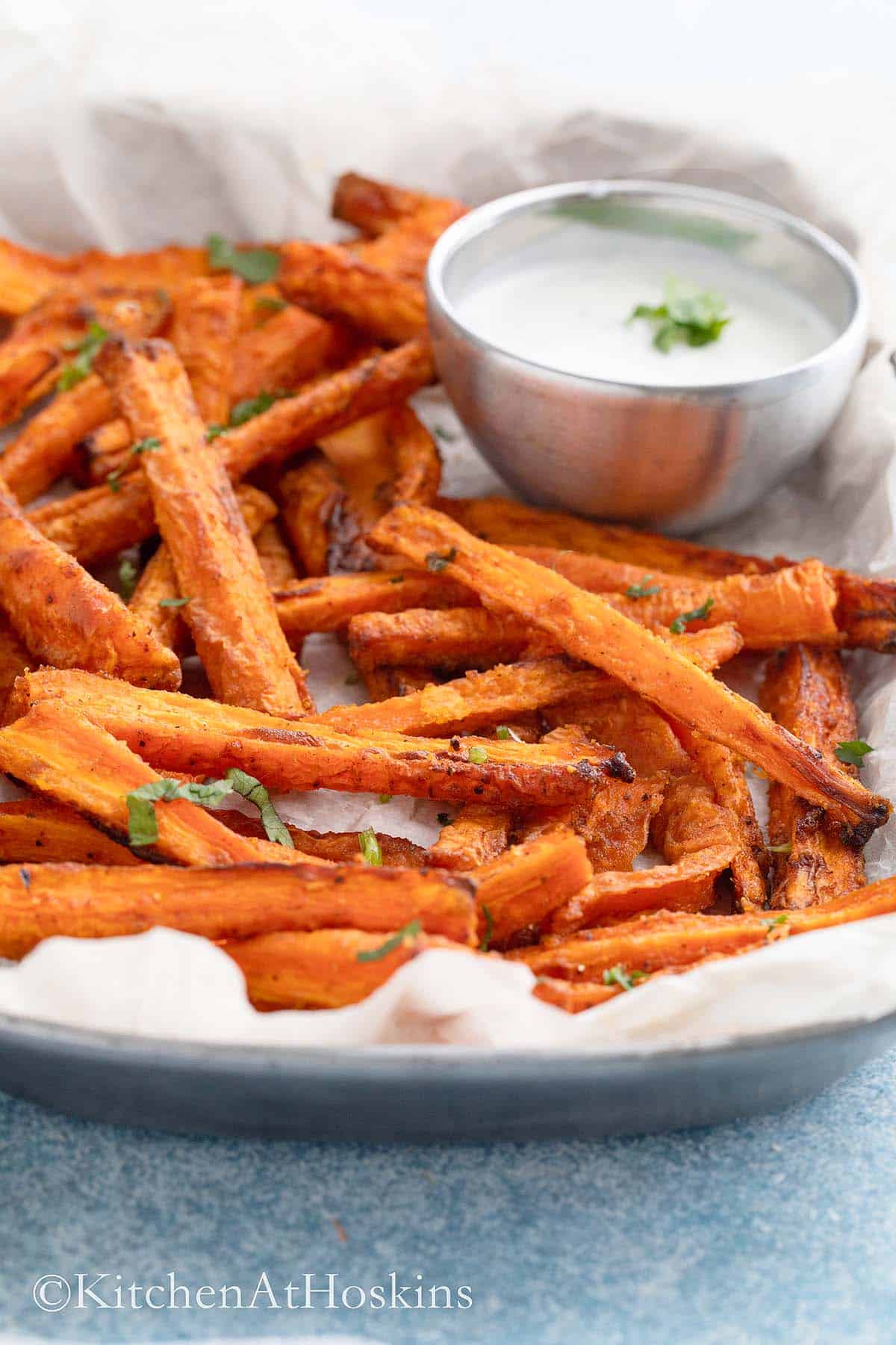 white parchment lined tray with cooked carrot fries and white sauce in a small bowl. 