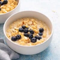 2 white bowls with quinoa porridge topped with blueberries.