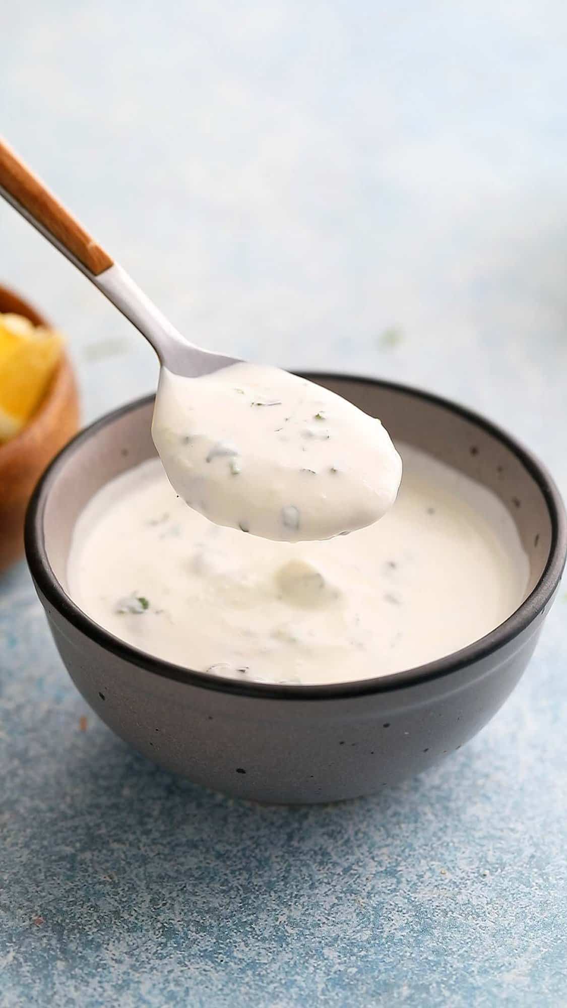 a spoonful of creamy white sauce above a grey bowl.