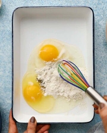 2 eggs, flour and seasonings in a white rectangle dish along with a whisk.