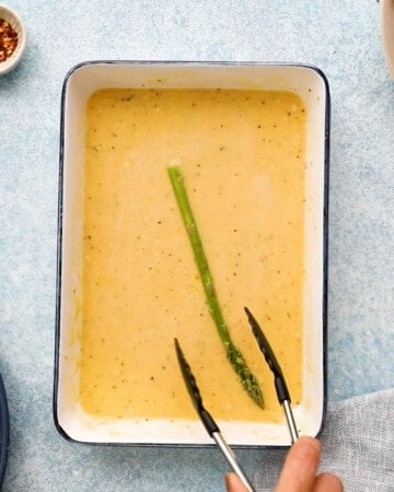 one green asparagus in yellow batter in a white rectangle dish.