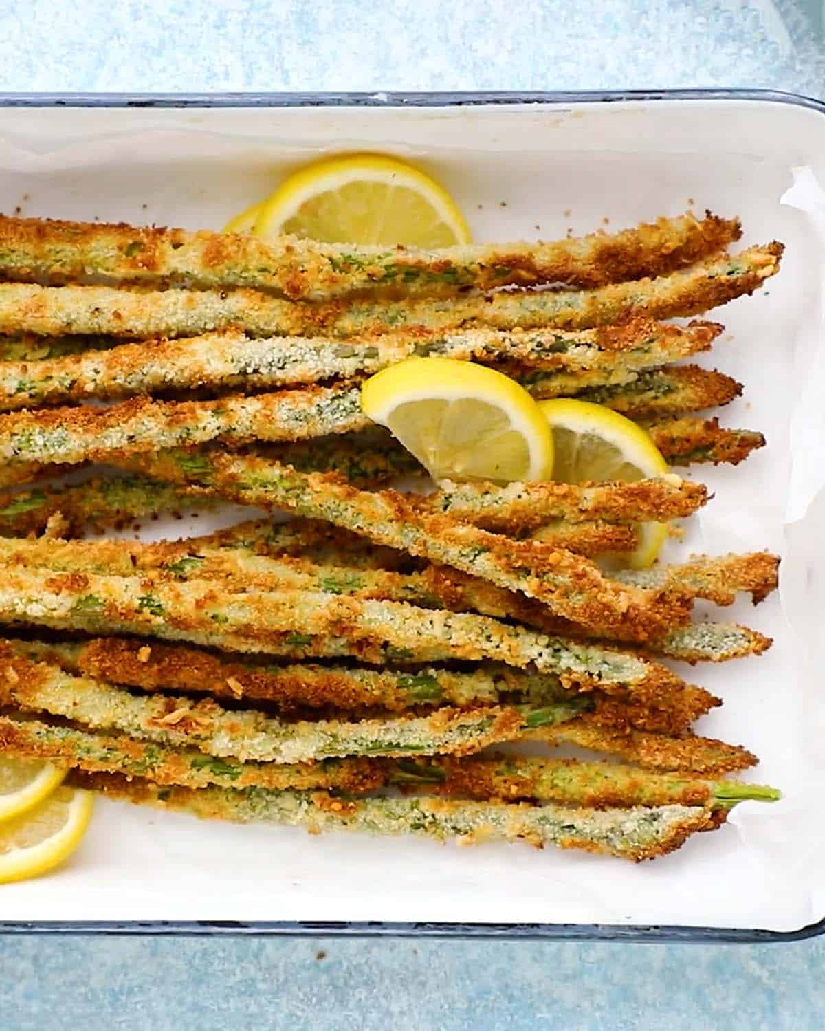 breaded asparagus fries along with lemon slices in a white rectangle dish.