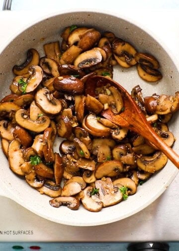 a hand sauteing sliced mushrooms in a small white skillet.
