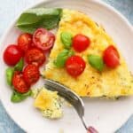 one slice of frittata on white plate with cut cherry tomatoes.