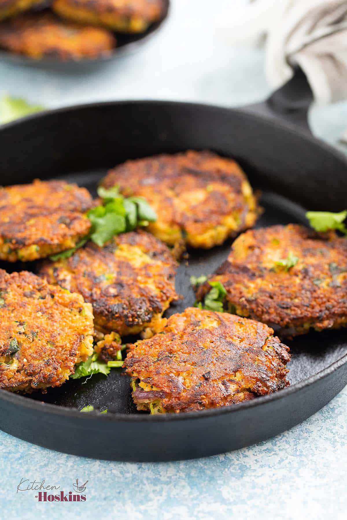 6 zucchini fritters in a black cast iron skillet.