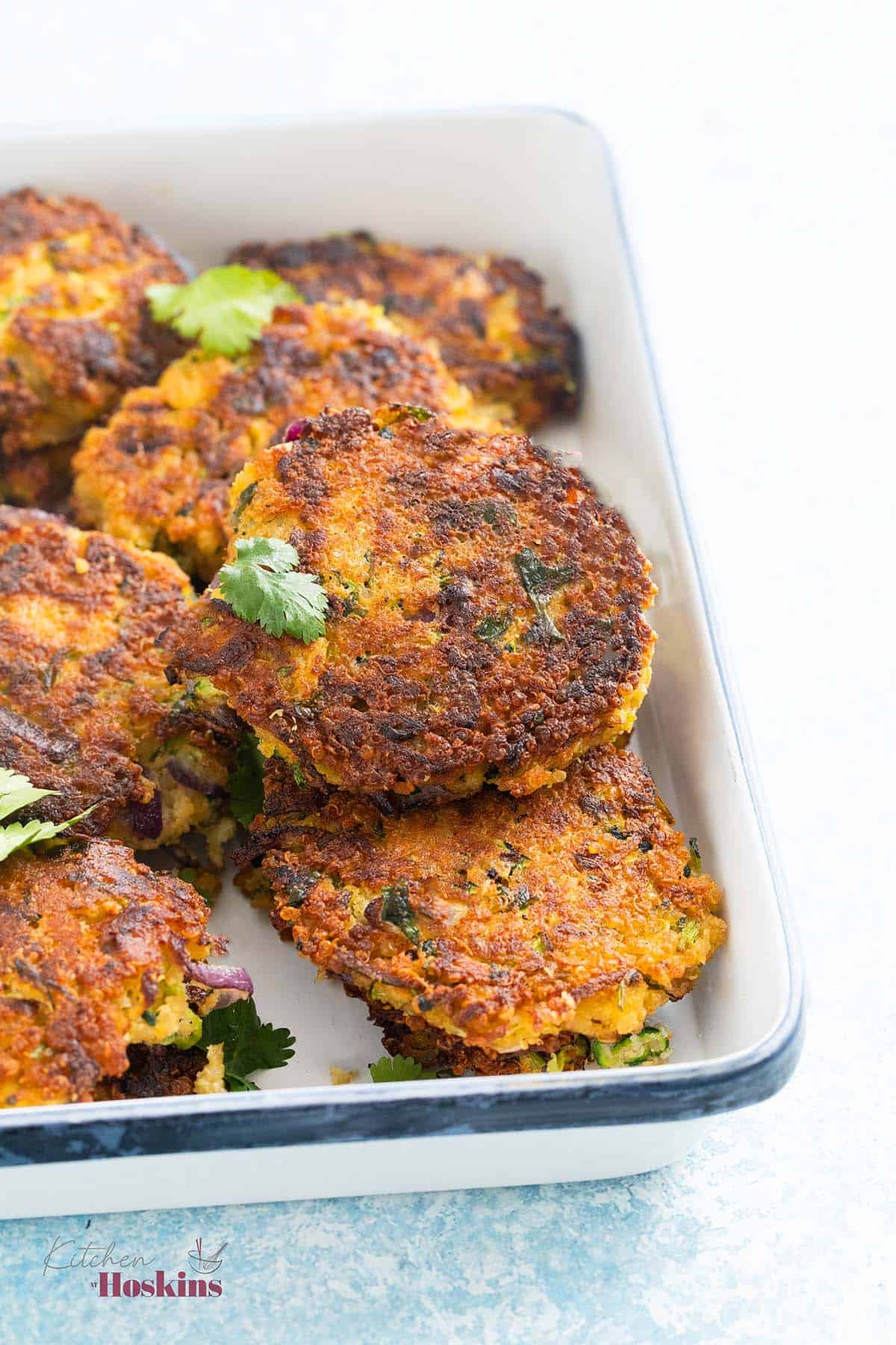 zucchini fritters piled in a white rectangular tray. 