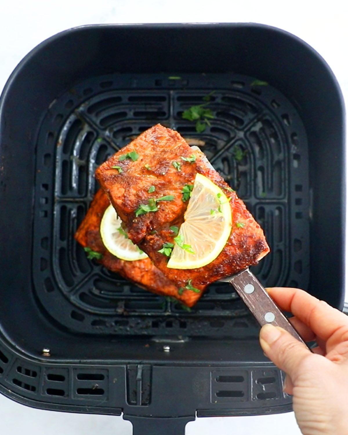 air fryer salmon with a lemon slice above a black air fryer basket.