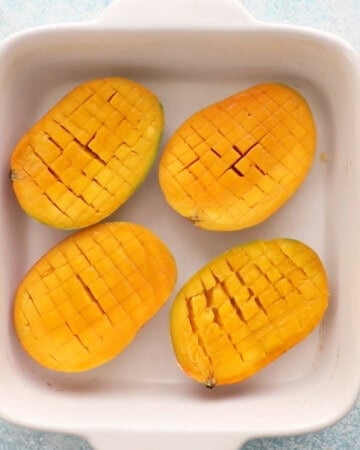 4 cut mangoes in a white baking dish.