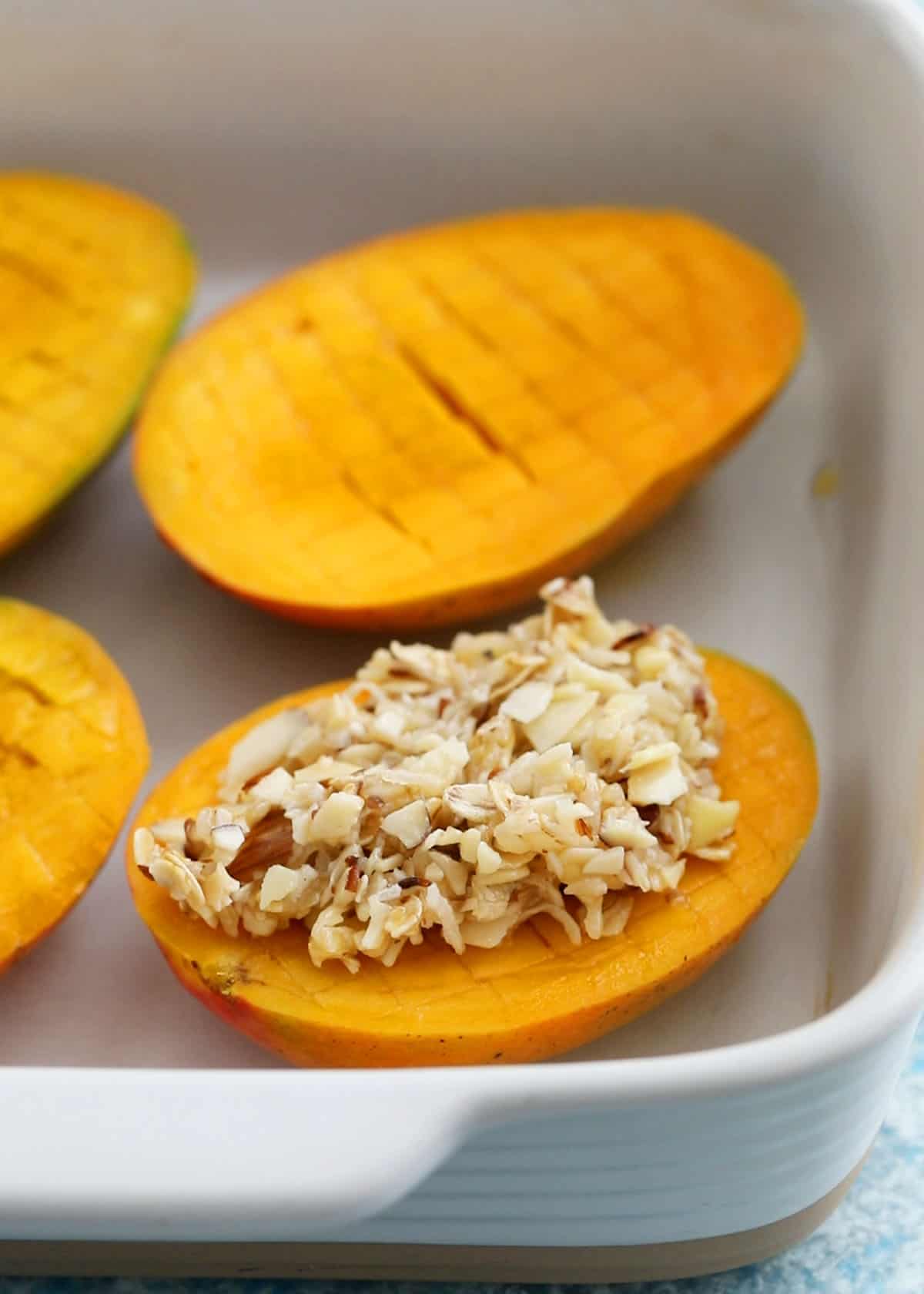 cut mangoes topped with coconut topping in a baking dish.