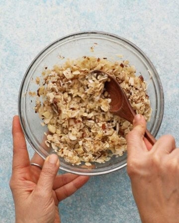 two hands mixing coconut filling in a glass bowl.