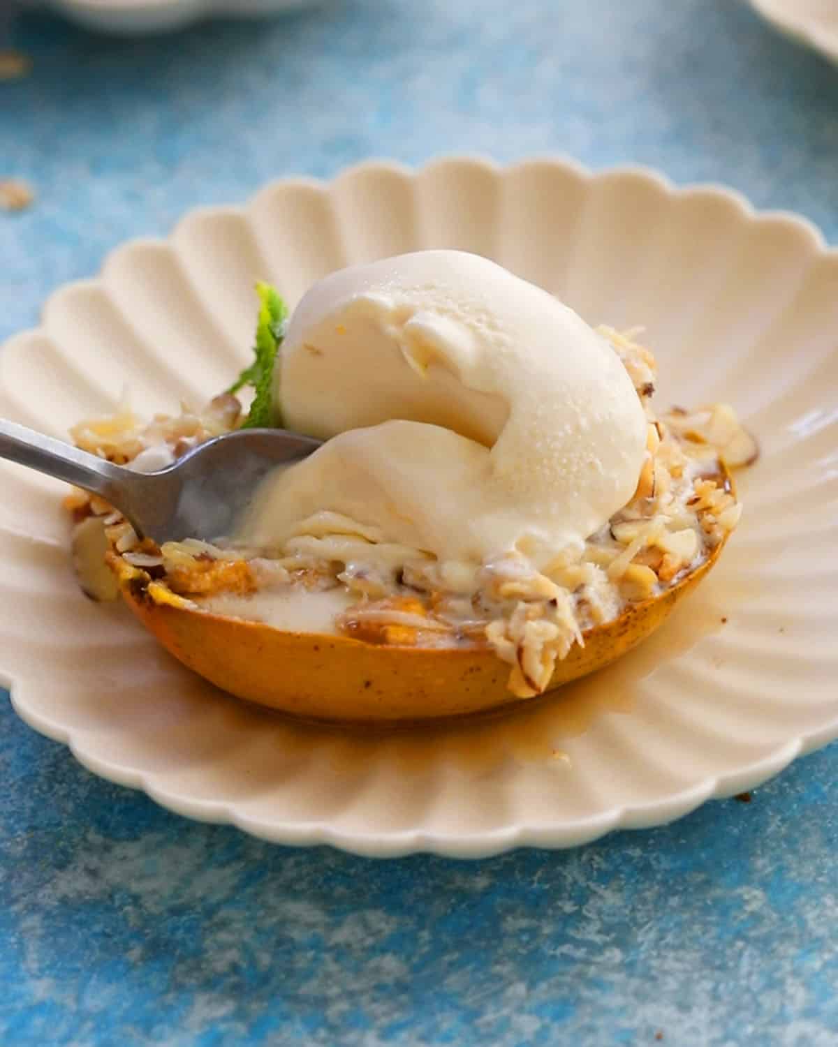 one baked mango topped with white ice cream in a fluted white plate.