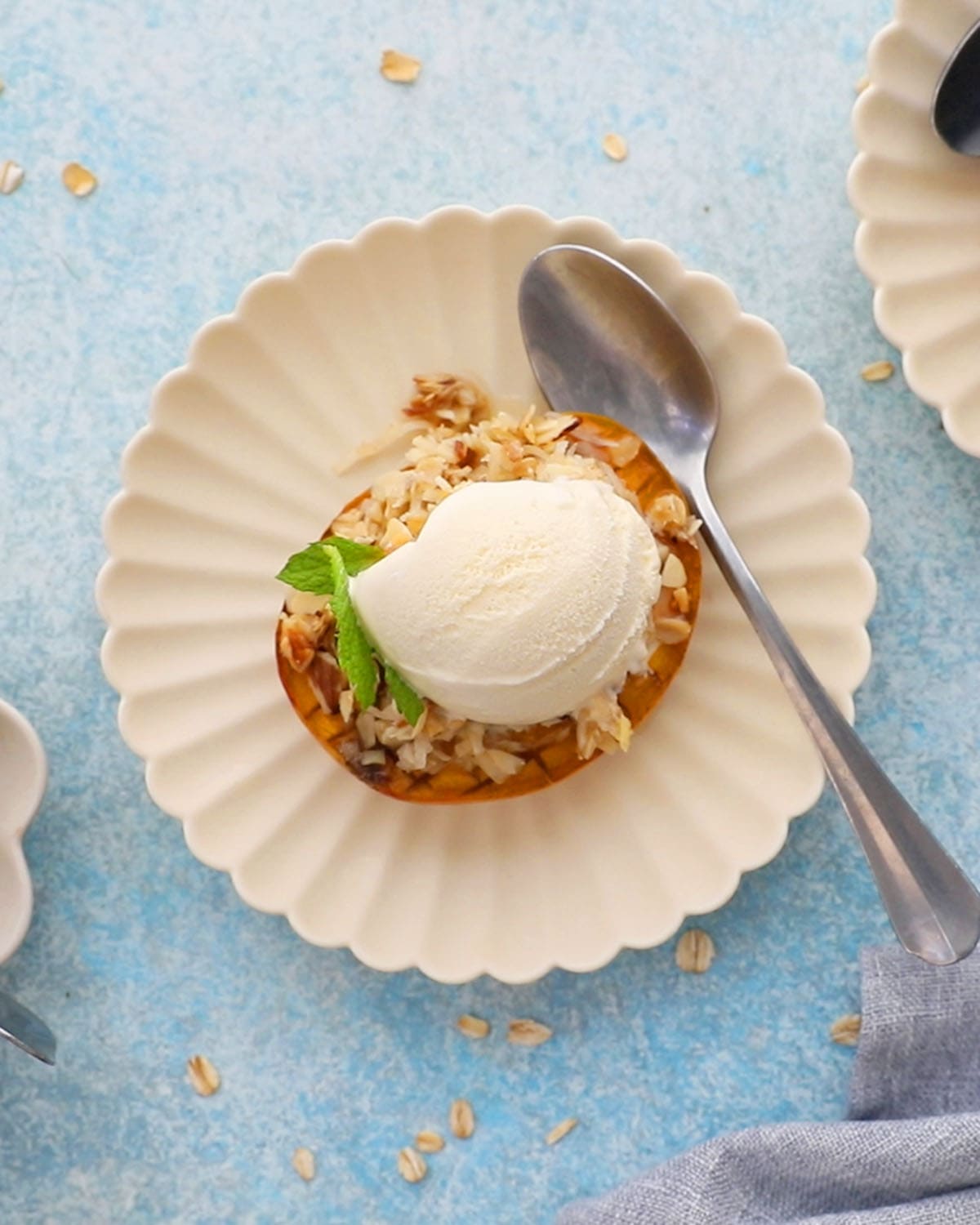 one baked mango topped with white ice cream in a fluted white plate.