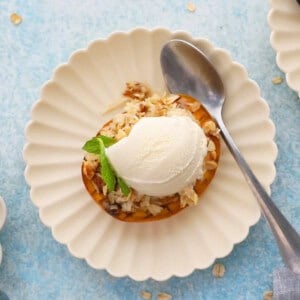 one baked mango topped with white ice cream in a fluted white plate.