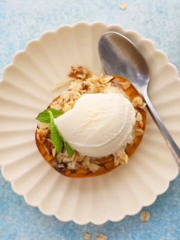 one baked mango topped with white ice cream in a fluted white plate.