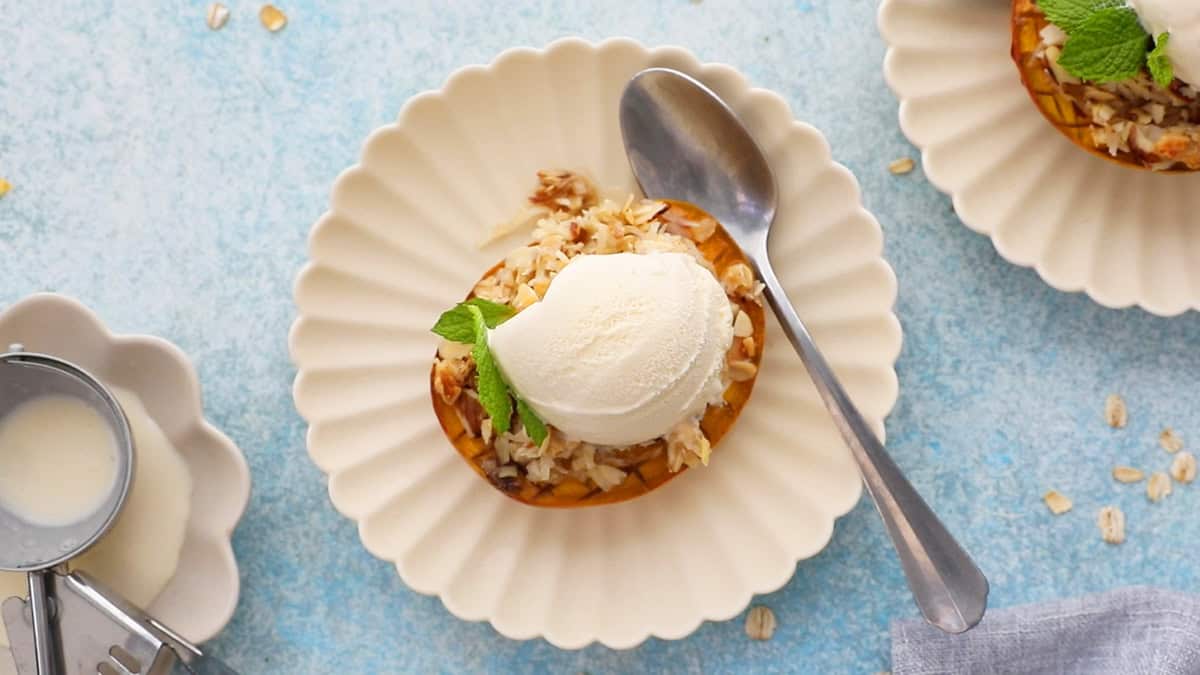 one baked mango topped with white ice cream in a fluted white plate.