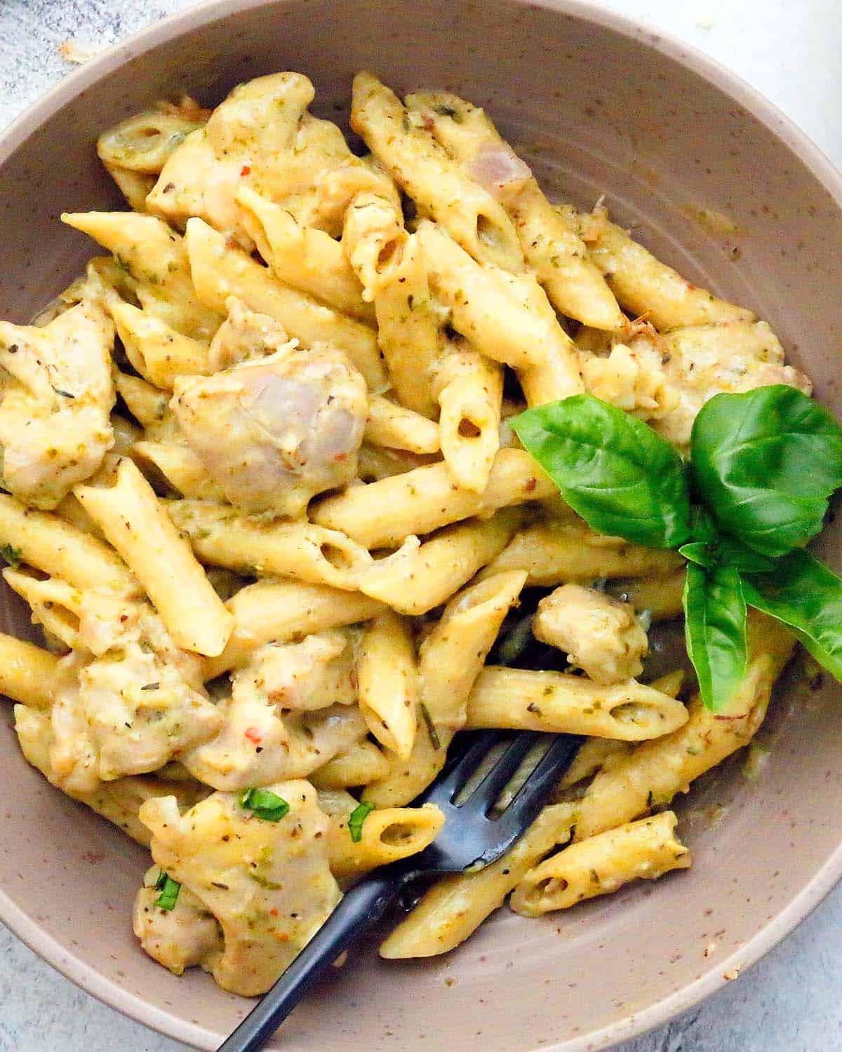 cooked penne pasta with chicken in a brown bowl along with a black fork.