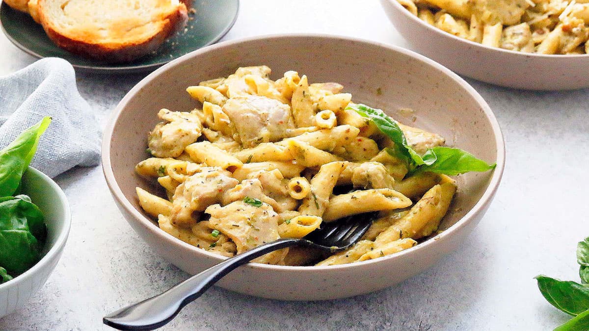 cooked penne pasta with chicken in a brown bowl along with a black fork.