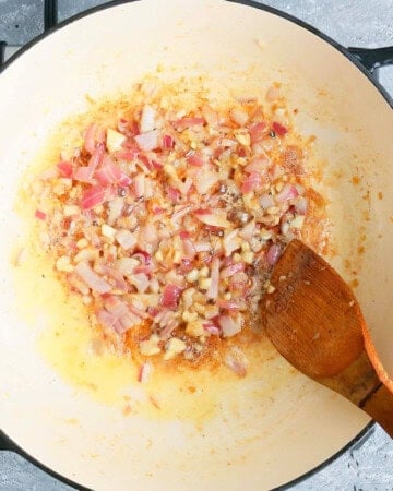 a hand cooking pink onion in a white pan.
