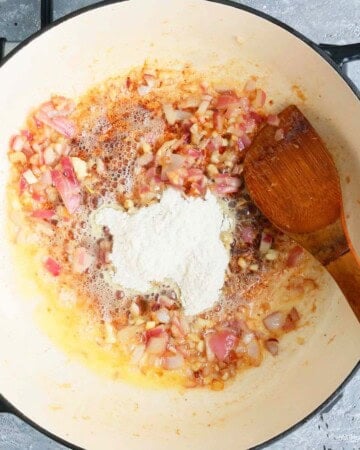 a hand cooking pink onion in a white pan.