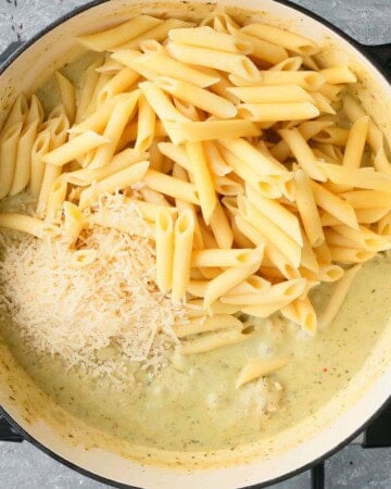 cooked penne pasta and green sauce in a white pan.